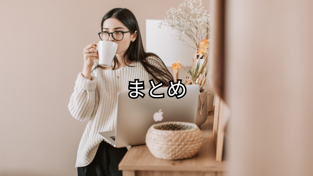 木の机に向かって立ってパソコン作業している女性が飲み物を飲んでいる